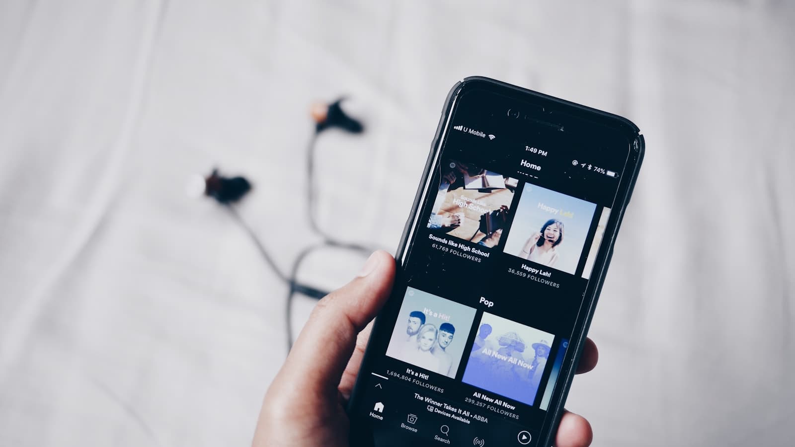 Hand holding a phone with a music streaming app open, earphones in the background